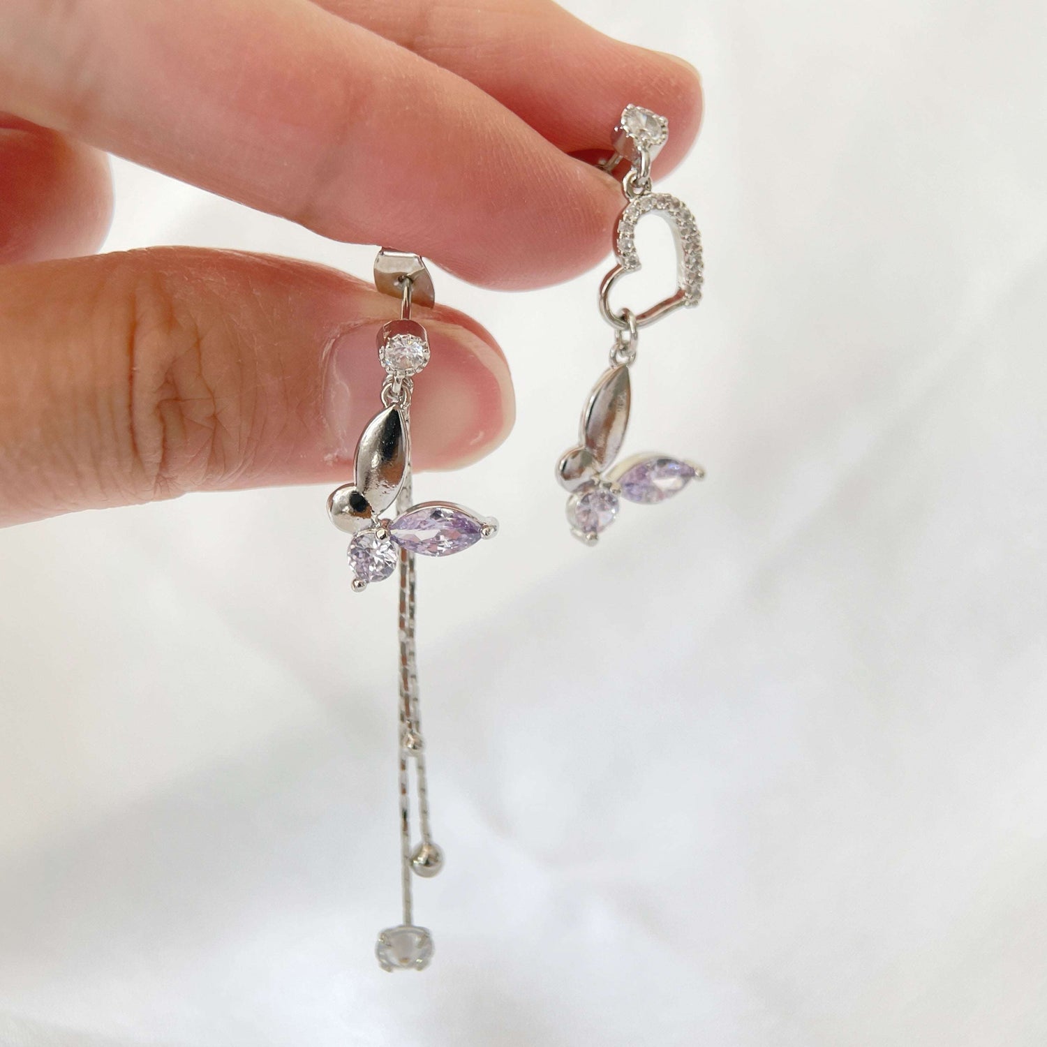 Pair of mismatched earring dangles in dream butterfly design crafted with semi-precious purple and colorless swarovski crystals, as well as a silver heart shape drops and two tassels drops - Sisilia Jewels