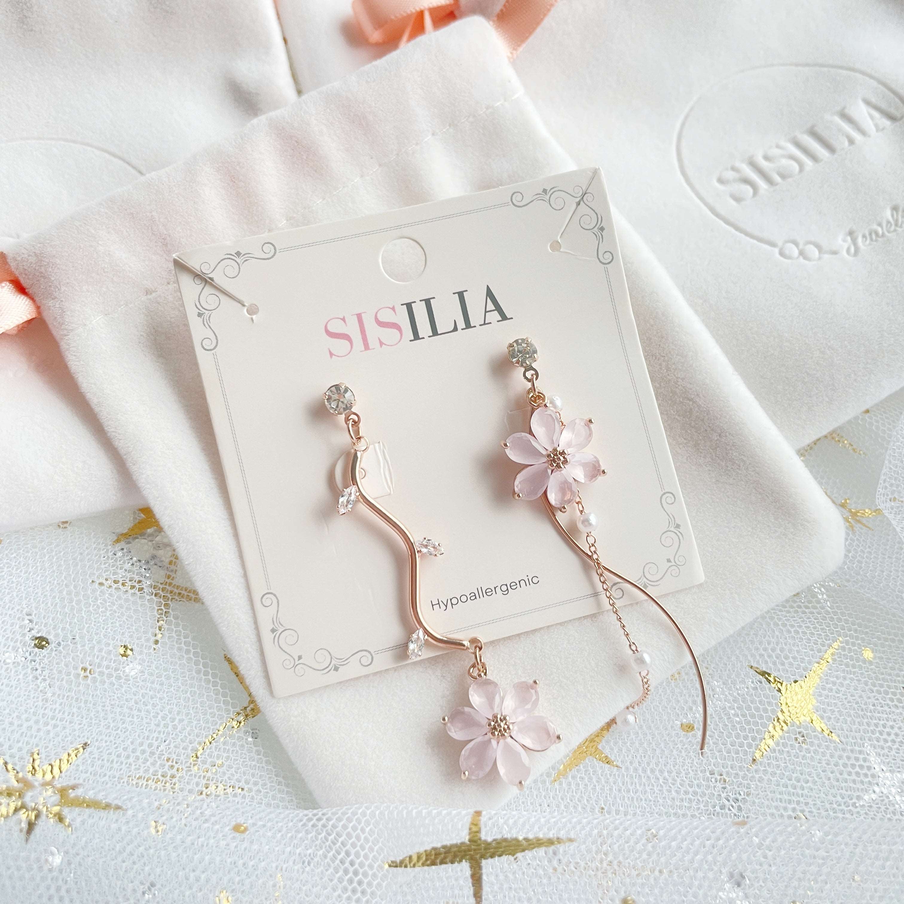 Mismatched earrings in six petals cute pink flower hanging on rose gold flower stems showcasing on jewelry bag - Sisilia Jewels