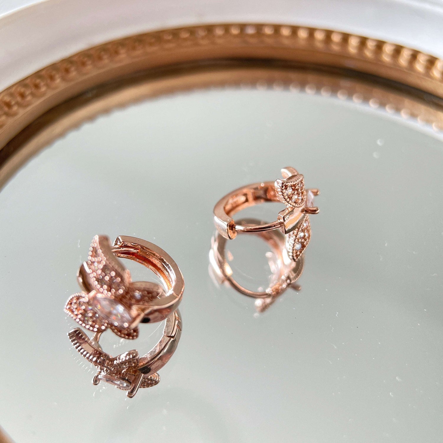 Pair of rose gold huggie earrings in butterfly design paved with cubic zirconia cz stones in one touch closure design on a mirror- Sisilia Jewels