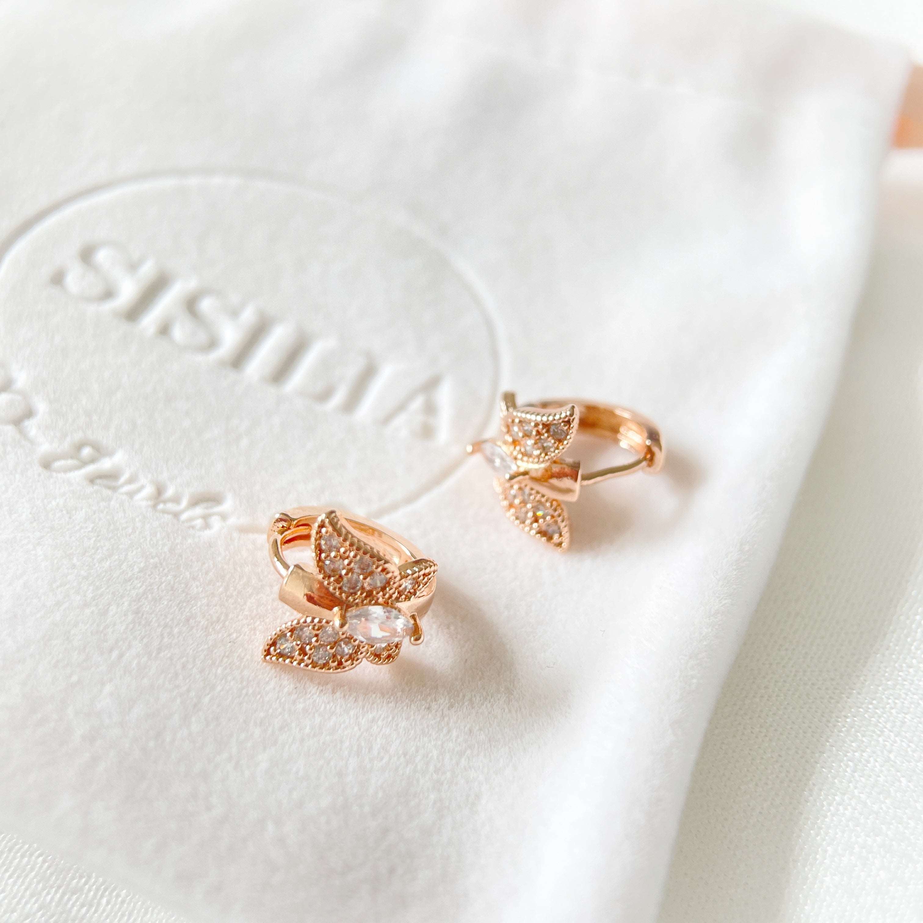 Pair of rose gold huggie earrings in butterfly design paved with cubic zirconia cz stones in one touch closure design on a jewelry bag - Sisilia Jewels